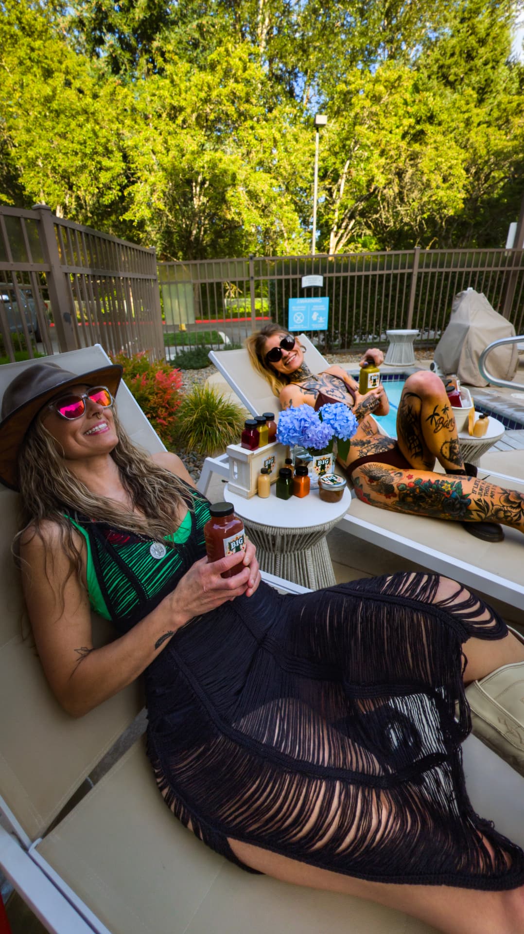 Tiffany relaxing poolside with a friend and bottles of BIG T Juice